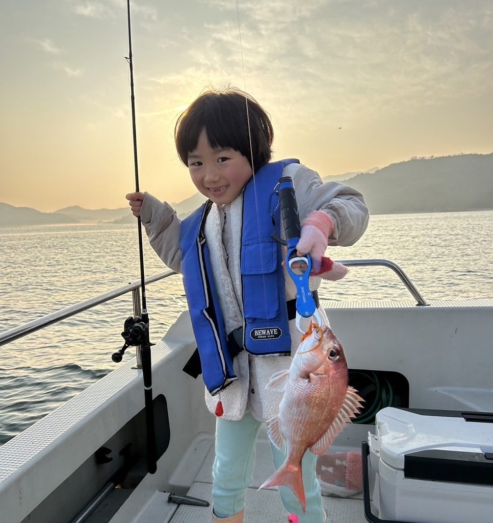 A child wearing a life jacket holds a freshly caught fish aboard a fishing boat on the Seto Inland Sea.