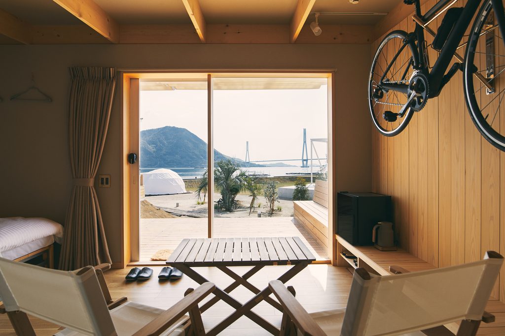 Interior of an ocean-view cottage at WAKKA, with wooden furnishings, a wall-mounted bicycle, and a view of the Seto Inland Sea.
